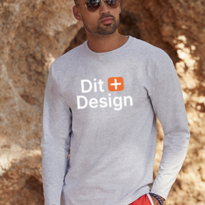 Mand i grå trøje står afslappet, iført solbriller og røde shorts, foran en klippevæg. Tekst på trøjen: "Dit Design".