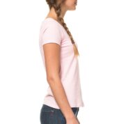 En kvinde med fletning står i profil, iført en lyserød T-shirt og mørke jeans, mod en hvid baggrund.