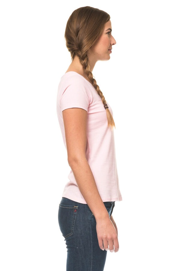 000210_Lady_Classic_04c En kvinde med fletning står i profil, iført en lyserød T-shirt og mørke jeans, mod en hvid baggrund.