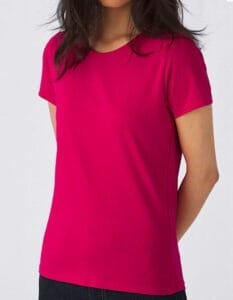En person iført en pink T-shirt står med armene bag ryggen i et neutralt, gråt rum. Ingen tekst er synlig.