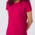 En person iført en pink T-shirt står med armene bag ryggen i et neutralt, gråt rum. Ingen tekst er synlig.