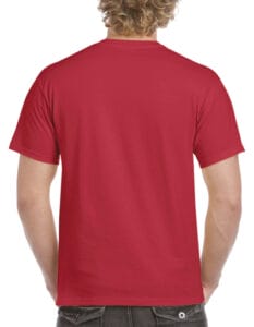 En person med lyst, krøllet hår står med ryggen mod kameraet iført en rød T-shirt og mørke jeans i en enkel, neutral baggrund.