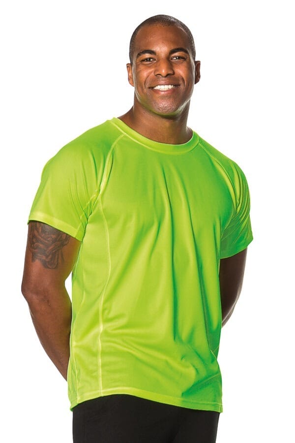 000350_Go_Sport_01c En mand iført en lys grøn T-shirt står og smiler, med hænderne foldet bag ryggen. Beklædningen er i et studie med en hvid baggrund.