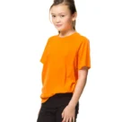 En person iført en orange T-shirt står og kigger fremad. De har sorte bukser på og befinder sig mod en hvid baggrund.