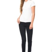 Person iført hvid polo-shirt, sorte bukser og sølvfarvede sneakers, smilende og stående oprejst i en minimalistisk, hvid baggrund.