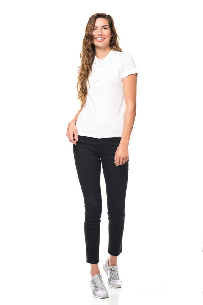 Person iført hvid polo-shirt, sorte bukser og sølvfarvede sneakers, smilende og stående oprejst i en minimalistisk, hvid baggrund.