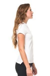 Kvinde iført en hvid T-shirt og sorte bukser står i profil mod en hvid baggrund, med langt bølget hår hængende ned over ryggen og ser fremad.