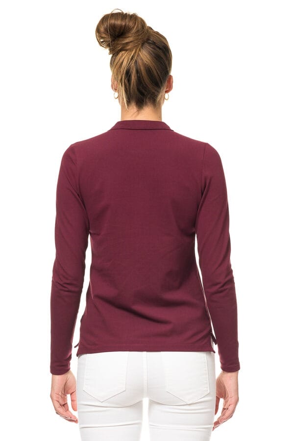 000810_Lady_Stretch_Polo_LS_03c_1 En person med samlet hår iført en vinrød trøje og hvide bukser står med ryggen til i et hvidt studie.