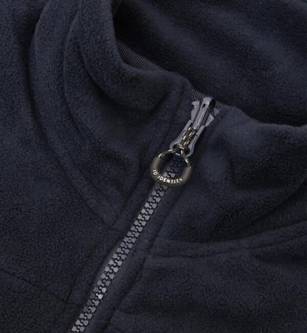 0811_790_pack_5 Mørkeblå fleecejakke med en halvt lynet lynlås. Lynlåsen har et sort vedhæng med teksten “ID IDENTITY”. Jakkens stof er blødt og struktureret.