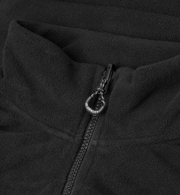 0811_900_pack_5 Sort fleecejakke med lynlås, hvorpå der står teksten "NO IDENTITY." Jakken er udbredt og viser en tæt detalje af lynlåsen i midten.