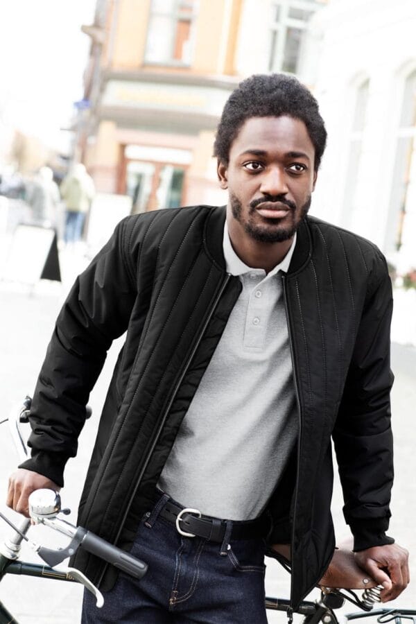 0886_900_image_1 Manden står med hænderne på et cykelstyr i en bymiljø. Han har en sort jakke og grå polo på, bygninger kan ses i baggrunden.