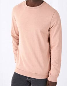 Mand iført beige sweatshirt med lange ærmer står med hænderne i lommerne af sorte bukser mod en hvid baggrund.