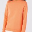 En person iført en lys orange sweatshirt står i en neutral lysegrå baggrund. Personen er skåret af ved halsen og bærer hvide bukser.