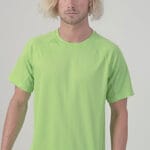 Mand med skulderlangt, lyst hår står stille iført en lys grøn T-shirt, set foran en neutral, lysegrå baggrund.