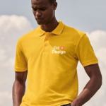 Person iført gul polo står udendørs; på trøjen står teksten "Dit + Design" i hvid skrift. Baggrunden er en delvist skyet himmel.