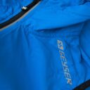 Blå jakke med lynlås og mærketekst "GEYSER" på siden, knap-lukning på lynlåsen, og syninger i stoffet.