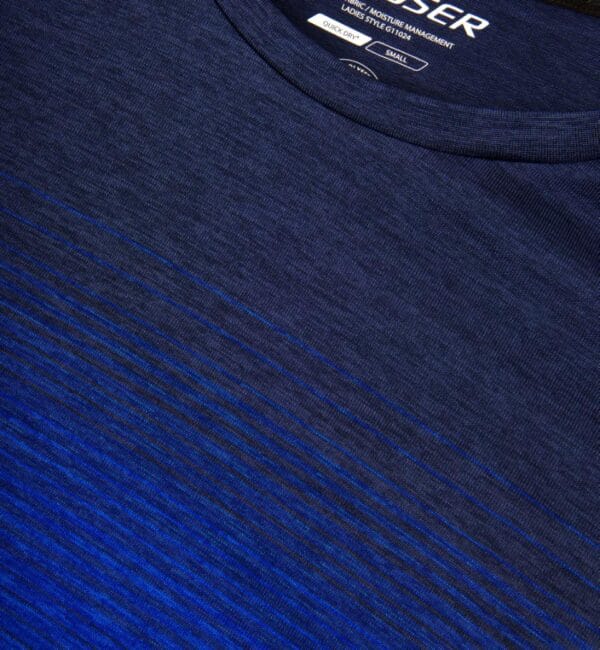 g11024_796_pack_5 En mørkeblå trøje med let graduerende striber nederst. Tekst på indersiden af trøjen læser: "LADIES MOISTURE MANAGEMENT LADIES STYLE G1024N QUICK DRY SMALL." Trøjen ligger fladt.