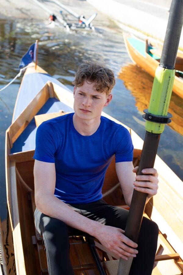 g21020_773_image_1 Mand sidder i en robåd og holder en åre. Baggrunden viser andre både i vandet og en bådebro. Han har en blå trøje på og ser alvorligt ud.