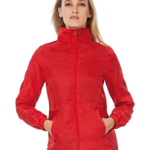 En person iført en rød jakke står med hænderne i lommerne mod en hvid baggrund. Jakken har en høj krave og lynlås fortil.