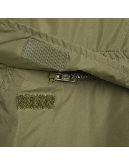 Lynlås lukker en grøn jakke i nærbillede, omgivet af velcro-stykker til justering og fastgørelse; stoffet ser glat og vandafvisende ud.