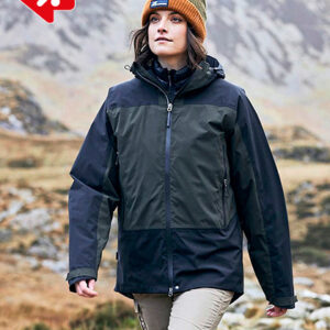 Person iført mørk jakke går i bjerglandskab med græsklædte bakker og stenbaggrund. Personens ansigt er ikke specificeret. Øverst til venstre ses en del af et rød-hvidt logo.