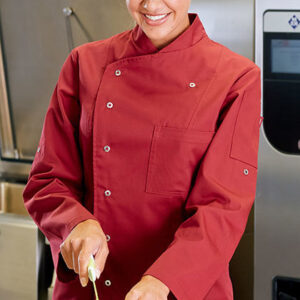 Kok iført rød kokkejakke skærer grøn peberfrugt på et bord i et professionelt køkken. Baggrunden viser køkkenudstyr og en stor ovn.