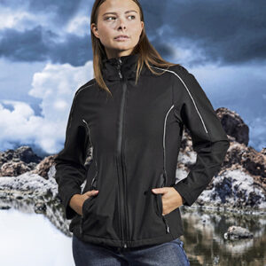 Person står iført en sort jakke med hænderne i lommerne og kigger mod venstre. Baggrunden består af skyet himmel og bjerge ved en sø.