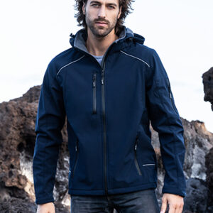 Mand bærer en mørkeblå jakke, står afslappet i udendørs klippeomgivelser. Han ser direkte mod kameraet, omgivet af stenet terræn og himmel bagved.