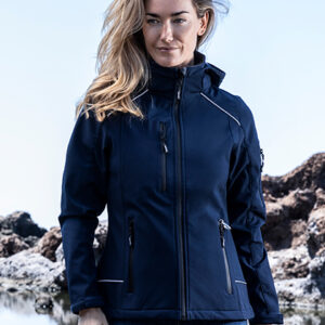 En person iført en mørkeblå jakke står udendørs. Personen har langt hår, og baggrunden er klippefyldt med lys himmel. Ingen tekst er til stede.