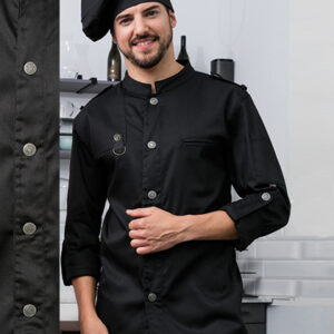 Kok iført sort kokkeuniform og sort baret smiler, mens han står i et køkkenmiljø med åbne hylder og køkkenredskaber i baggrunden.