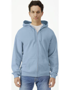 En person iført en lyseblå hættetrøje står stille; trøjen er lynet op, og personen har en hvid T-shirt indenunder mod en lys baggrund. Ingen tekst er til stede.