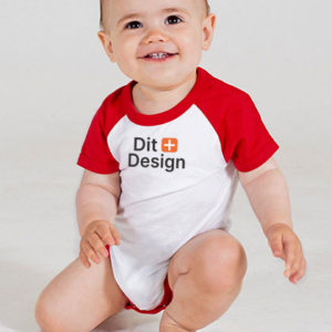 Et lille barn sidder på gulvet iført en rød-hvid bodystocking. Der står "Dit Design" på tøjet. Barnet smiler i et neutralt, lyst rum.