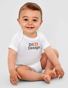 En lille baby sidder og smiler på en neutral baggrund, iført en hvid sparkedragt med teksten "Dit + Design" på brystet.