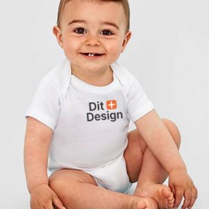 En lille baby sidder og smiler på en neutral baggrund, iført en hvid sparkedragt med teksten "Dit + Design" på brystet.
