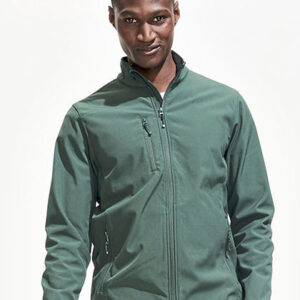 Person iført en mørkegrøn jakke står afslappet med hænderne i lommerne, i et neutralt oplyst rum med hvid baggrund.