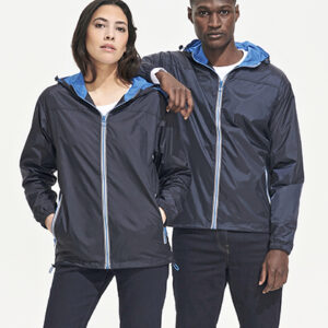 To personer står sammen iført mørkeblå jakker med lynlås og hætte, begge med hænderne i lommerne. Baggrunden er lys og ensfarvet.