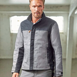 En person iført en grå jakke står i et rum med lys indretning. Baggrunden har store vinduer, som slipper naturligt lys ind.