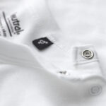 Hvid t-shirt ligger udfoldet med en sort mærkeseddel og to sølvknapper ved halsåbningen. Tekst: "Neutral Certified Responsibility" og "100% Organic Cotton".