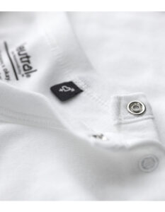 Hvid t-shirt ligger udfoldet med en sort mærkeseddel og to sølvknapper ved halsåbningen. Tekst: "Neutral Certified Responsibility" og "100% Organic Cotton".