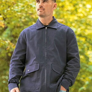 Mand iført en mørk jakke går gennem en skovklædt park på en solrig dag. Han kigger opad, omgivet af grønne træer og lysende løv.