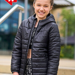 Jeg kan ikke identificere personer på billeder. En person i en sort, quiltet jakke står udendørs og smiler. Baggrunden viser en moderne glasbygning og grønne træer.