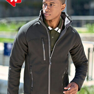 Mand iført sort jakke går udendørs i solrigt miljø med slørede bygninger i baggrunden.