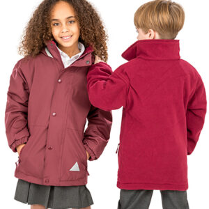 To børn iført røde jakker; den ene kigger fremad, den anden vender ryggen til. De står i et neutralt, lyst rum. Ingen tekst er til stede.