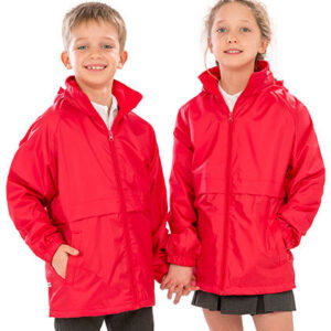 To børn iført røde jakker står sammen og holder hinanden i hånden. De smiler begge og har hvide trøjer under jakkerne. Baggrunden er enkel og lys.