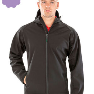 Mand iført sort jakke står oprejst. Han har hænderne i jakkens lommer. Baggrunden er enkel med en lilla form øverst i venstre hjørne.