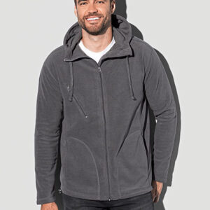 En mand iført en grå jakke med hætte står stille mod en lys baggrund. Jakken har lynlås og lange ærmer. Han smiler. Der er ingen tekst i billedet.