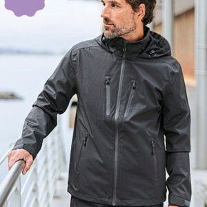 Mand iført sort jakke står på en balkon, ser ud over vandet. Bygninger og en bro kan anes i baggrunden. Tekst: "NEW" i en lilla mærkat i øverste venstre hjørne.