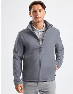 Mand bærer en grå softshell-jakke, står afslappet med hånden i lommen. Under jakken er en grå polotrøje synlig. Baggrunden er simpel og lys.