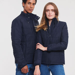 To personer iført mørkeblå jakker står ved siden af hinanden. De ser direkte frem. Baggrunden er ensfarvet lys.