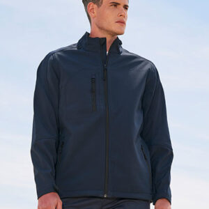 En person iført en mørk jakke står udenfor. Jakken har en lynlås og lommer på forsiden. Baggrunden viser en lyseblå himmel. Personen kigger mod højre.